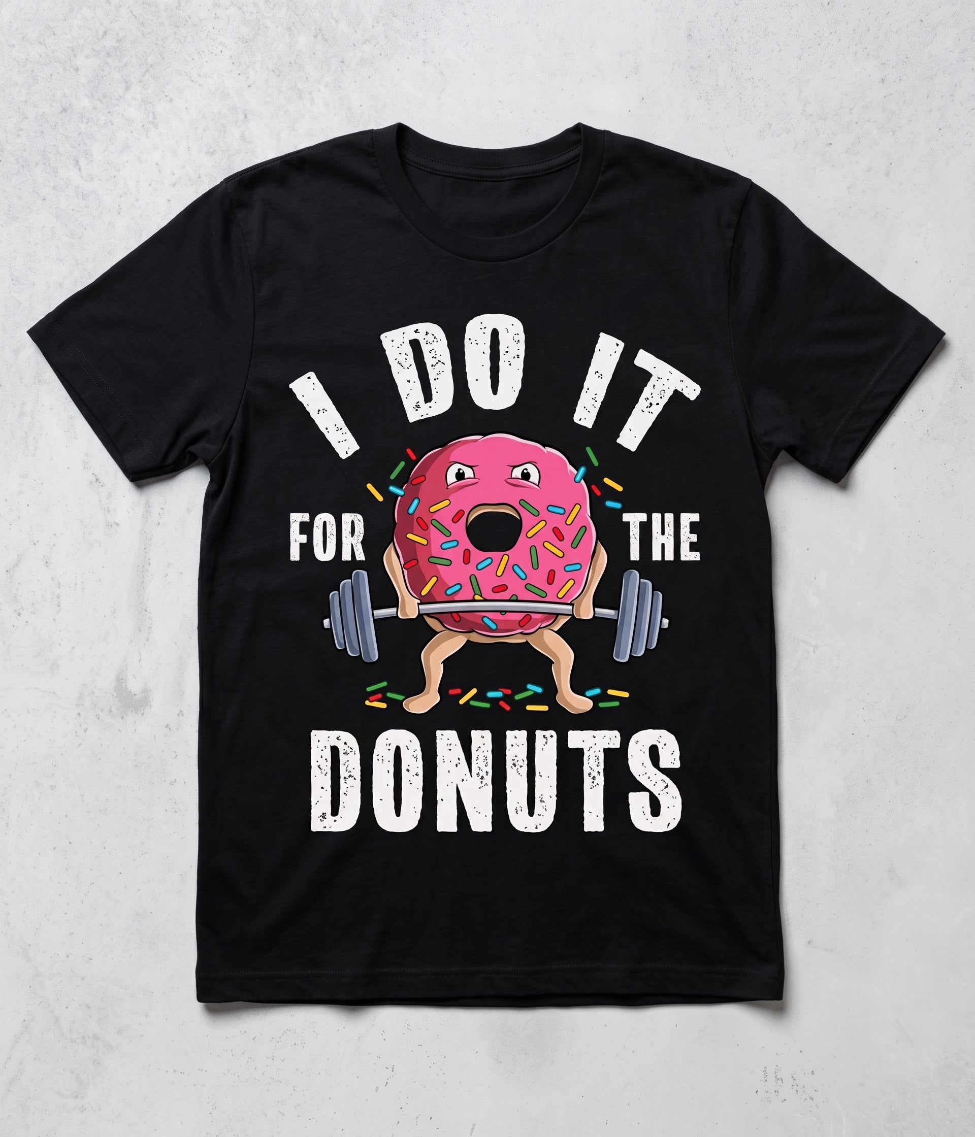 A black short-sleeve t-shirt with a graphic print of a cartoon pink donut lifting a barbell, surrounded by the text 'I DO IT FOR THE DONUTS' in white distressed lettering, displayed on a light gray textured background.